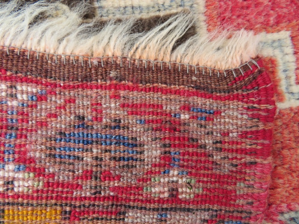 An antique hand-knotted Turkish Mujur wool rug featuring a stepped central medallion on a red field with patterned borders and fringed edges. View V