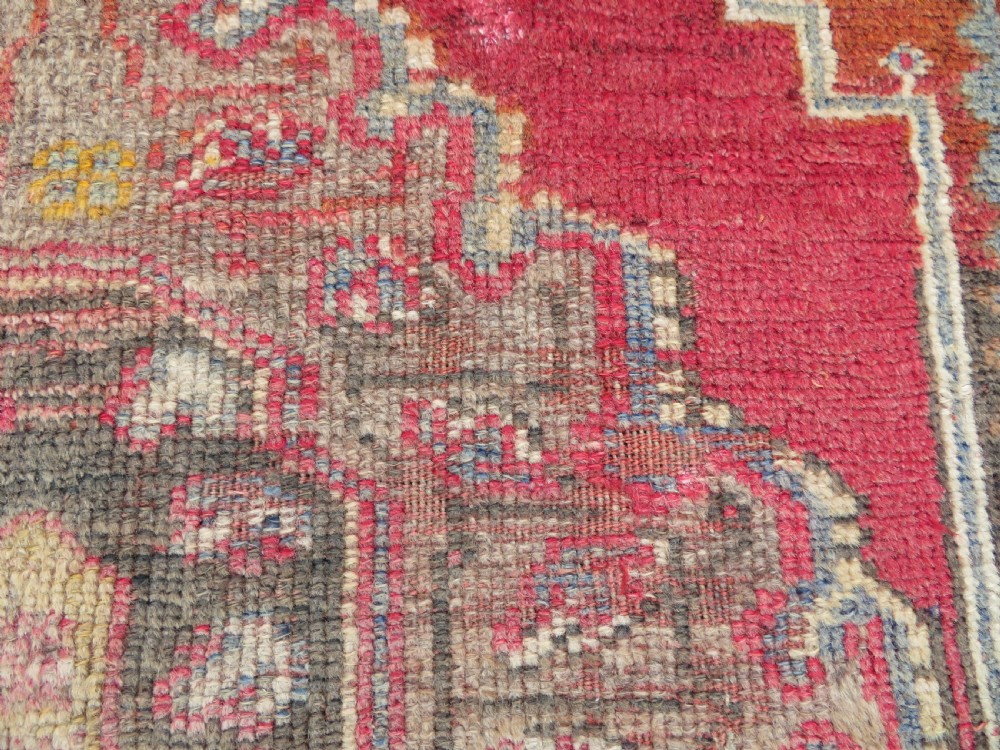 An antique hand-knotted Turkish Mujur wool rug featuring a stepped central medallion on a red field with patterned borders and fringed edges. View VI