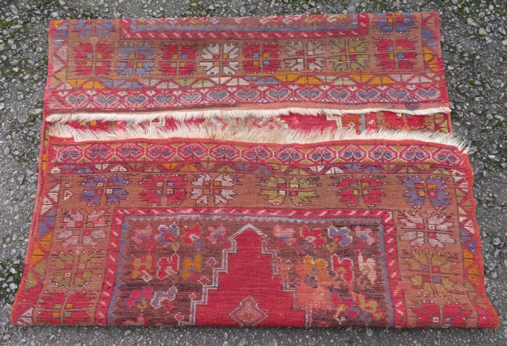 An antique hand-knotted Turkish Mujur wool rug featuring a stepped central medallion on a red field with patterned borders and fringed edges. View X