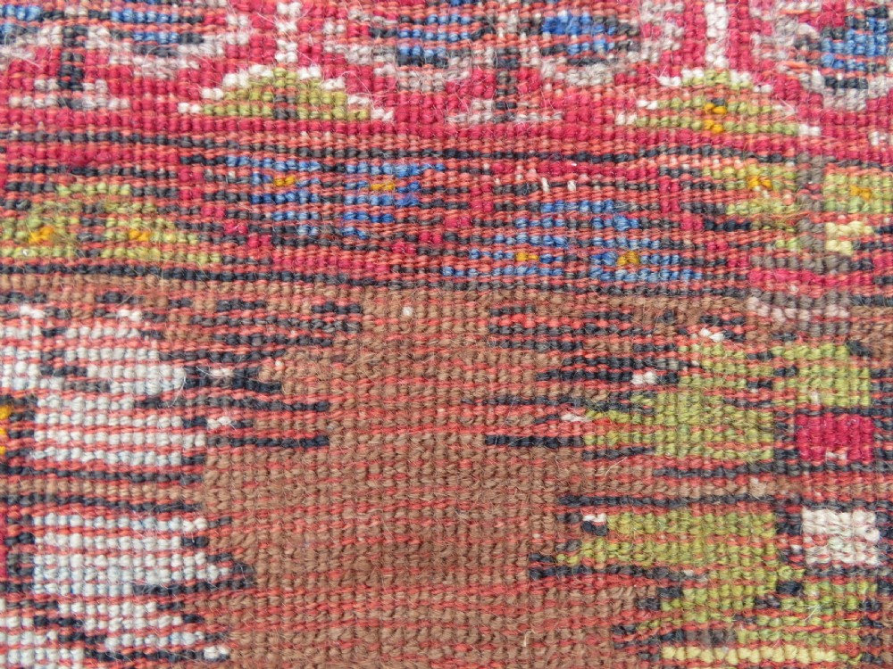 An antique hand-knotted Turkish Mujur wool rug featuring a stepped central medallion on a red field with patterned borders and fringed edges. View XII