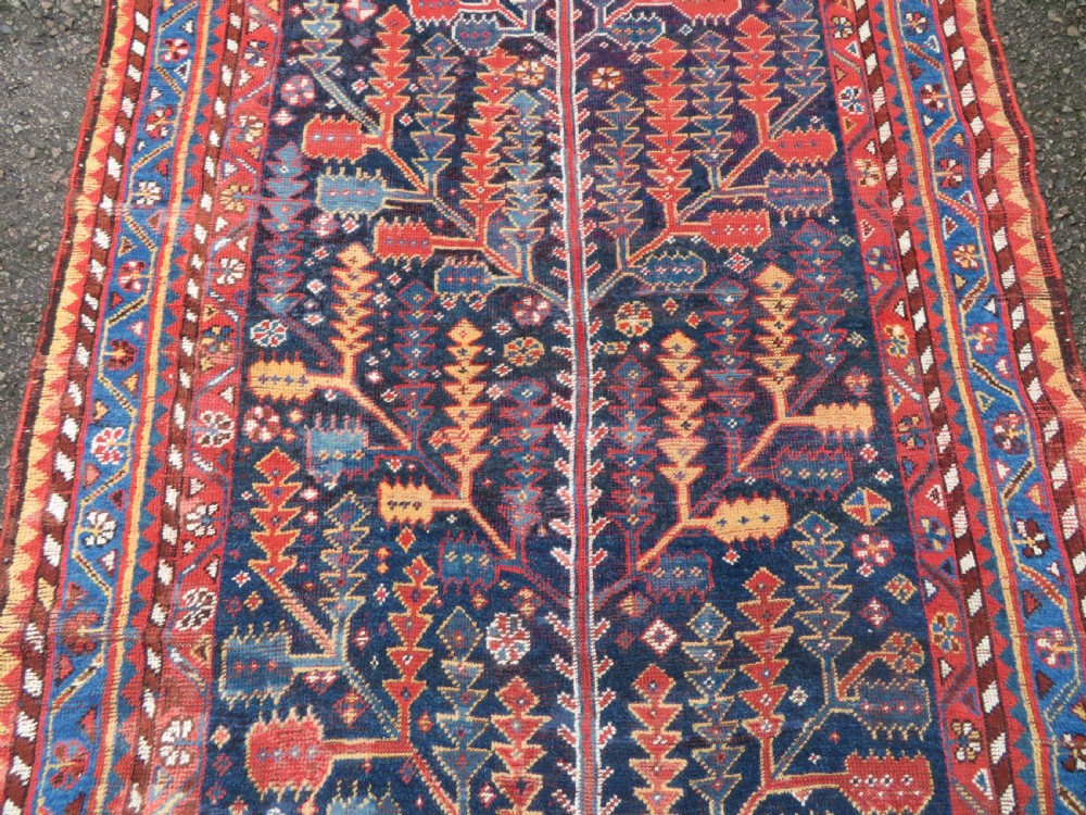 An antique hand-knotted wool kelleh rug featuring a central tree of life motif in red, yellow, and light blue against a dark navy field. View III