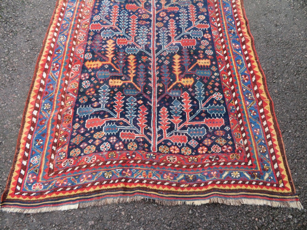 An antique hand-knotted wool kelleh rug featuring a central tree of life motif in red, yellow, and light blue against a dark navy field. View V