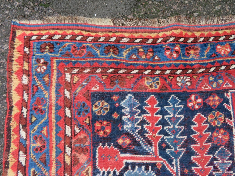 An antique hand-knotted wool kelleh rug featuring a central tree of life motif in red, yellow, and light blue against a dark navy field. View IX