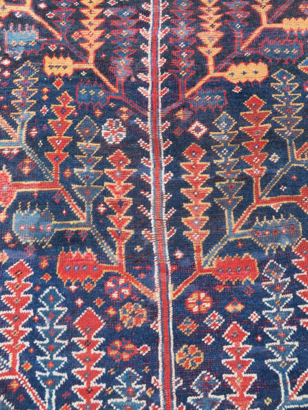 An antique hand-knotted wool kelleh rug featuring a central tree of life motif in red, yellow, and light blue against a dark navy field. View XII