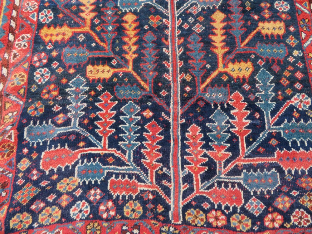 An antique hand-knotted wool kelleh rug featuring a central tree of life motif in red, yellow, and light blue against a dark navy field. View XIII