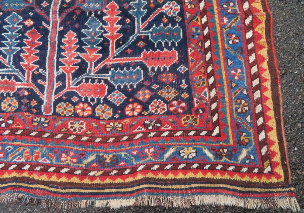 An antique hand-knotted wool kelleh rug featuring a central tree of life motif in red, yellow, and light blue against a dark navy field. View XIV