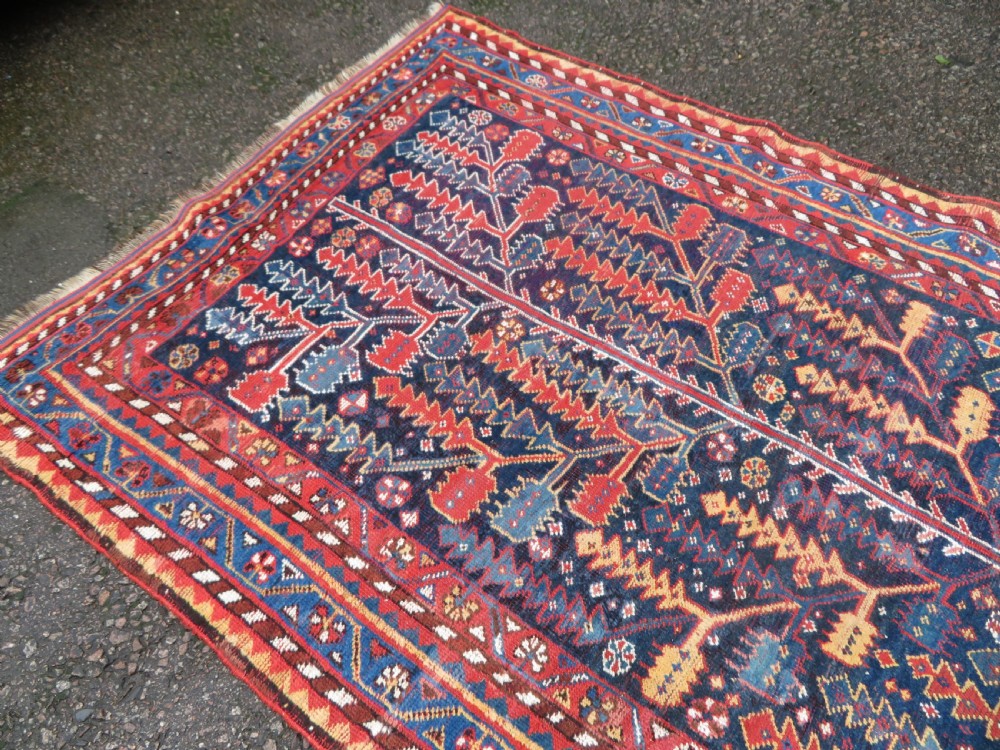 An antique hand-knotted wool kelleh rug featuring a central tree of life motif in red, yellow, and light blue against a dark navy field. View XV