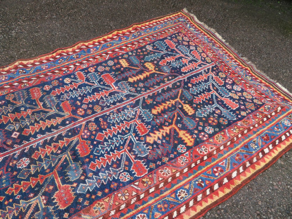 An antique hand-knotted wool kelleh rug featuring a central tree of life motif in red, yellow, and light blue against a dark navy field. View XVI