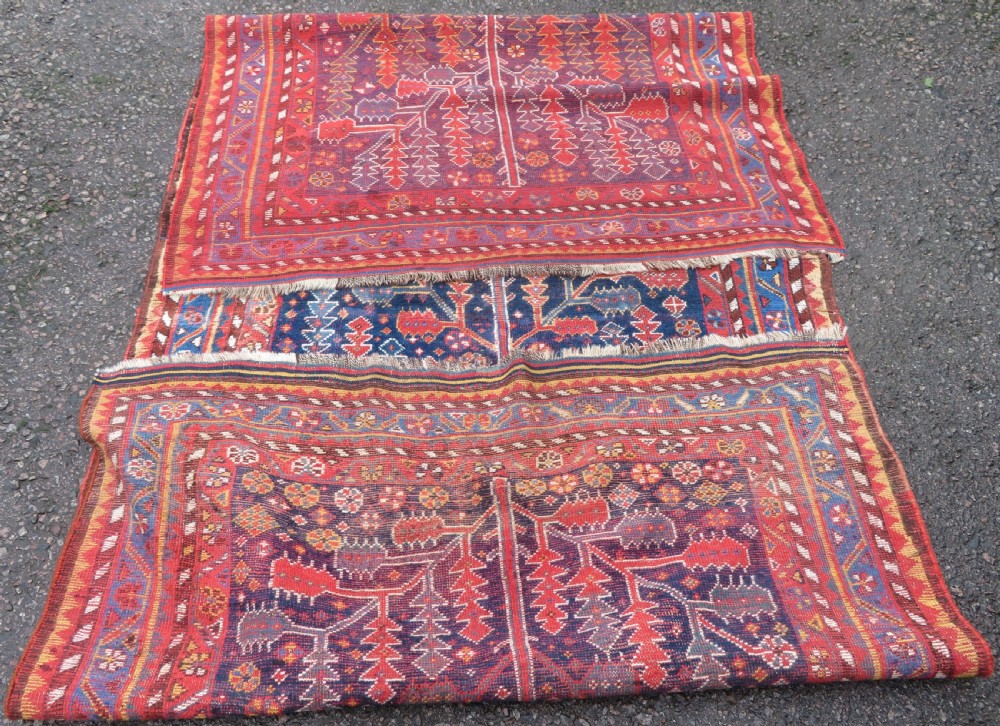An antique hand-knotted wool kelleh rug featuring a central tree of life motif in red, yellow, and light blue against a dark navy field. View XVII