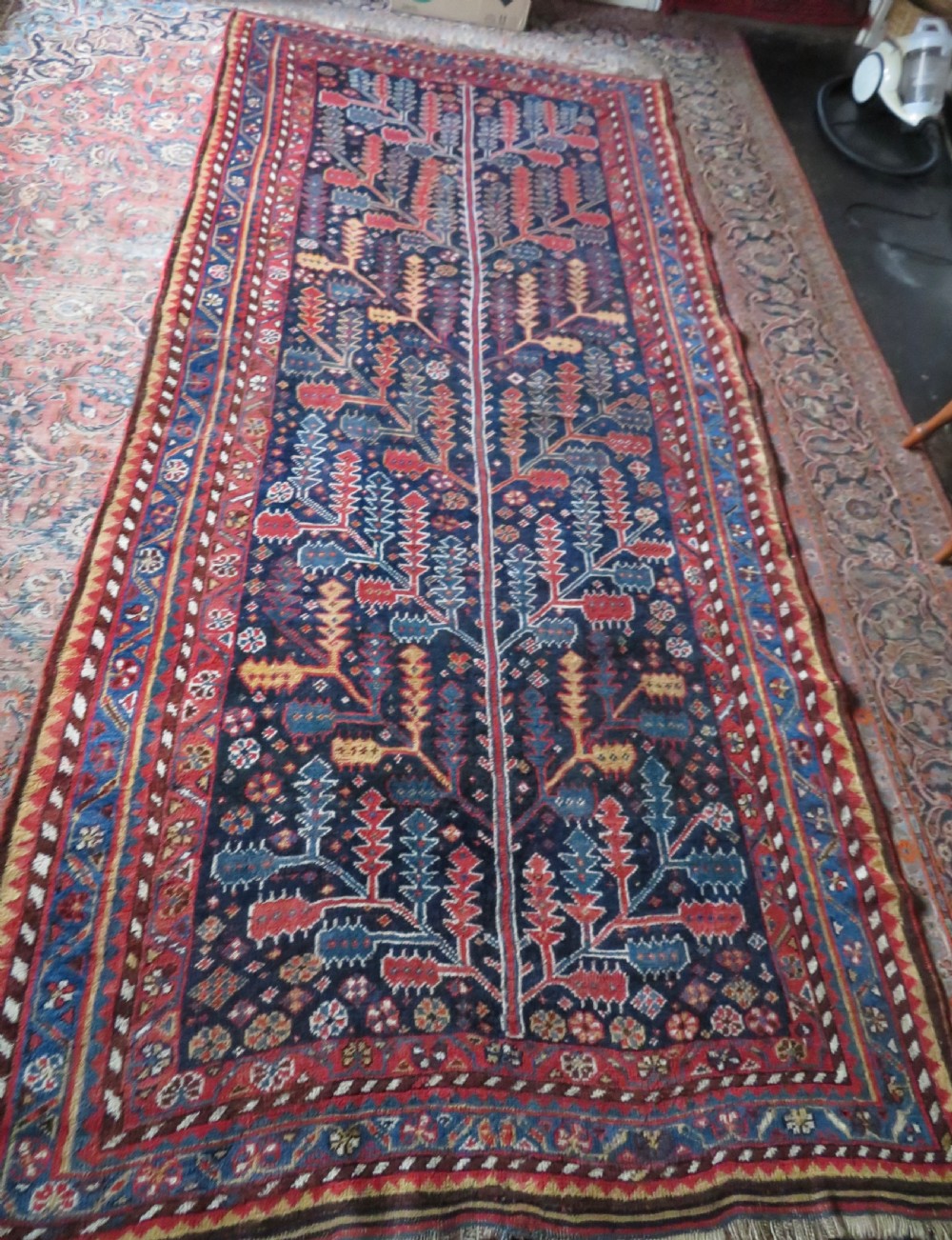 An antique hand-knotted wool kelleh rug featuring a central tree of life motif in red, yellow, and light blue against a dark navy field. View XXI