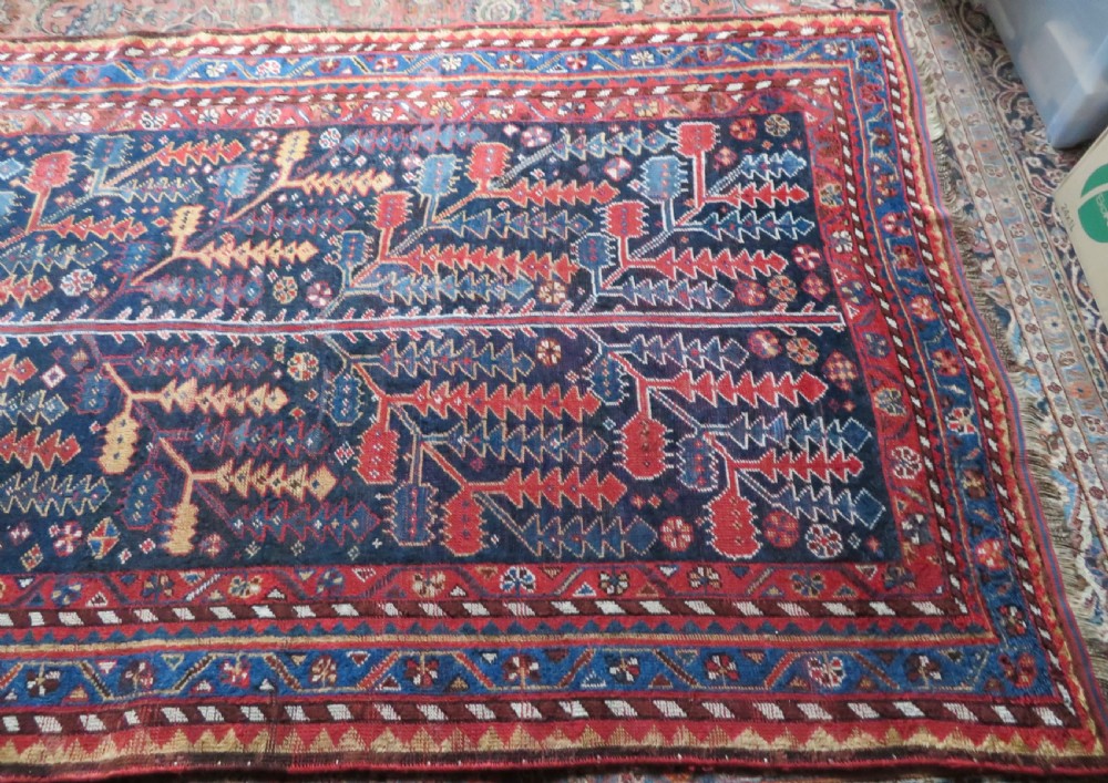 An antique hand-knotted wool kelleh rug featuring a central tree of life motif in red, yellow, and light blue against a dark navy field. View XXIII