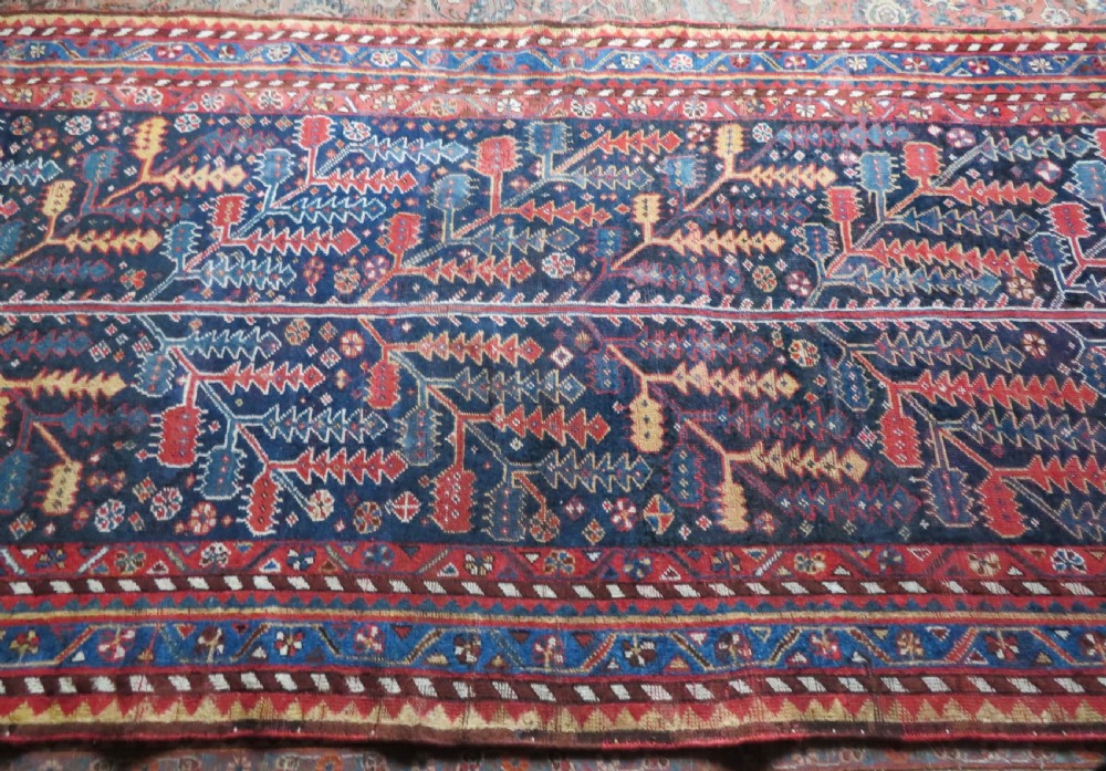 An antique hand-knotted wool kelleh rug featuring a central tree of life motif in red, yellow, and light blue against a dark navy field. View XXIV
