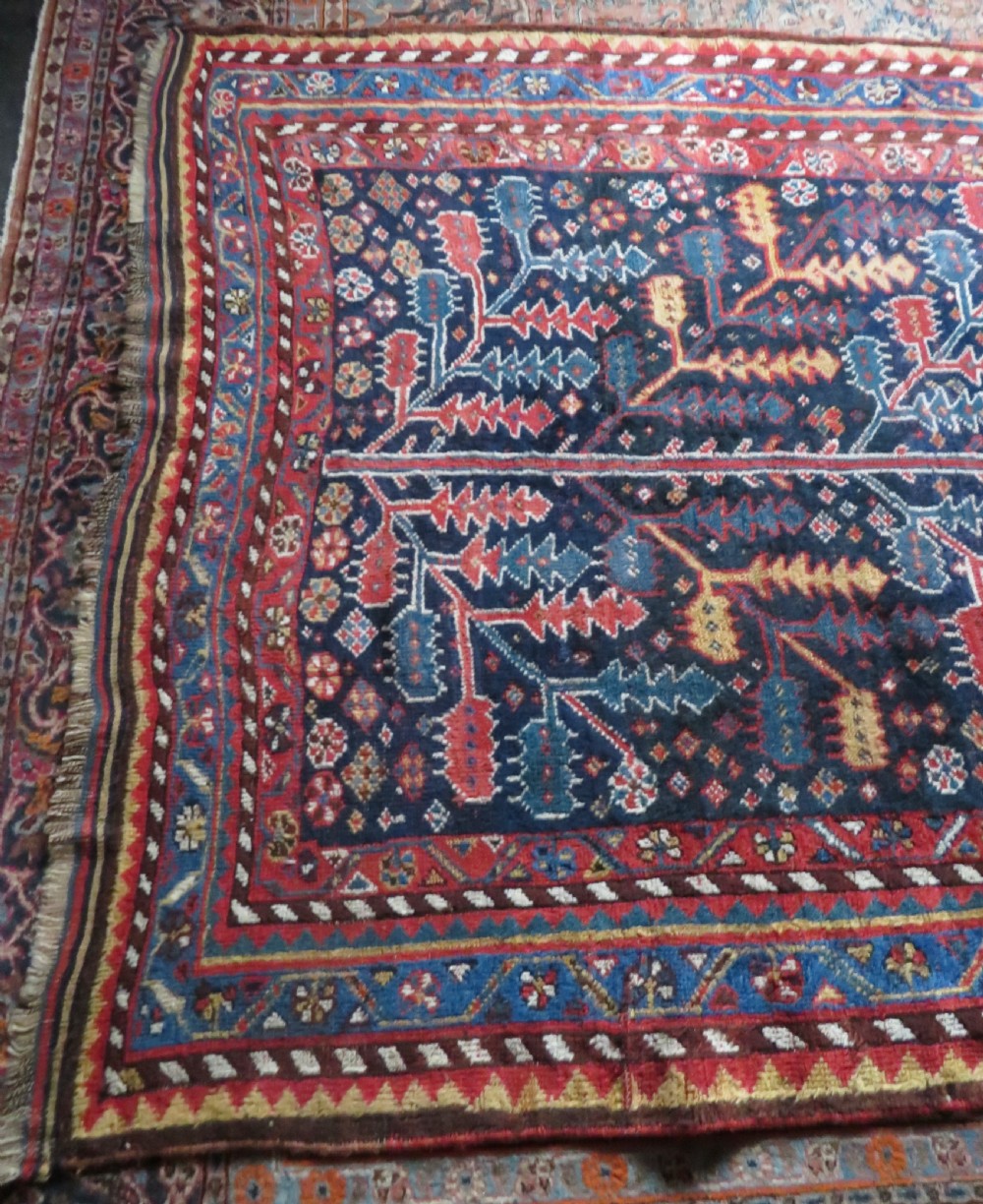 An antique hand-knotted wool kelleh rug featuring a central tree of life motif in red, yellow, and light blue against a dark navy field. View XXV
