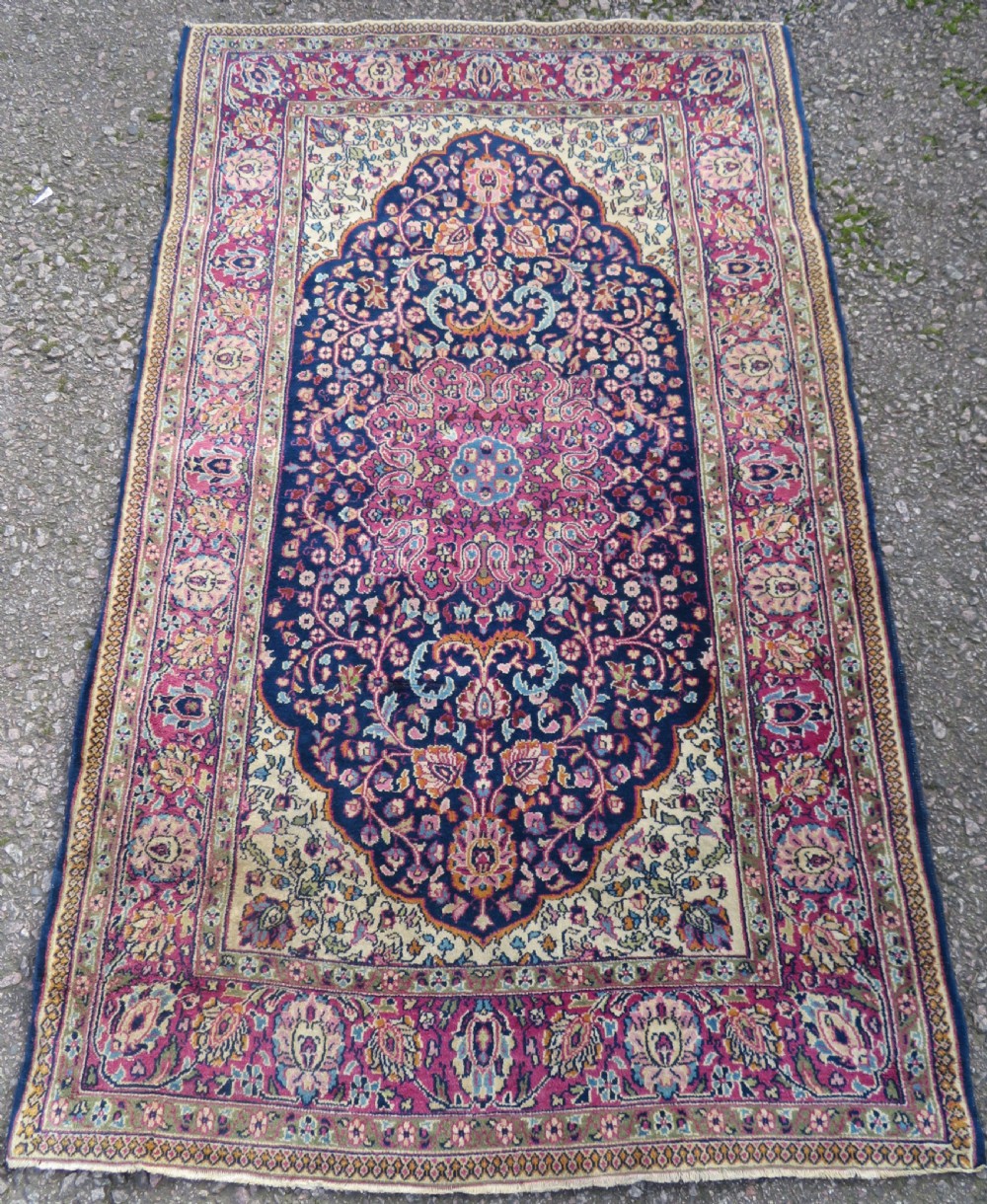 A rectangular hand-knotted wool rug featuring a central indigo floral medallion, cream spandrels, and a magenta border.