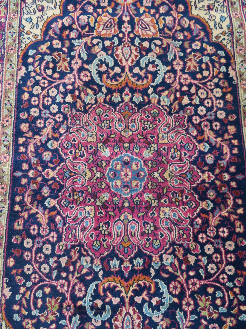 A rectangular hand-knotted wool rug featuring a central indigo floral medallion, cream spandrels, and a magenta border. View II