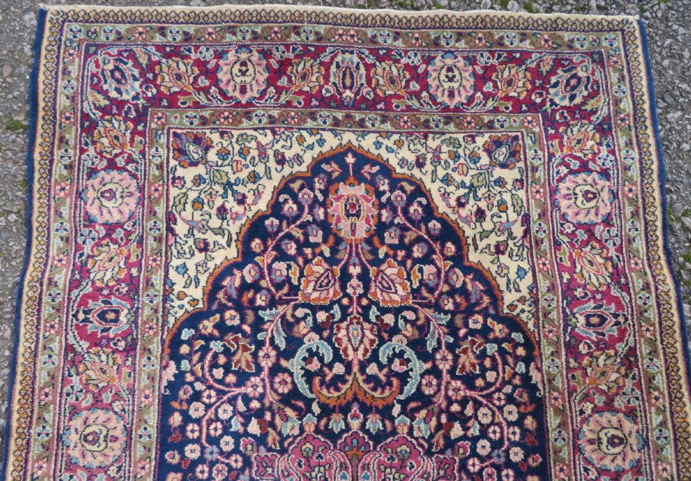 A rectangular hand-knotted wool rug featuring a central indigo floral medallion, cream spandrels, and a magenta border. View IV