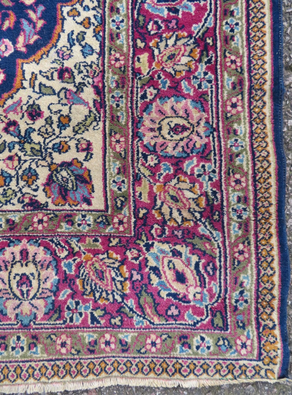 A rectangular hand-knotted wool rug featuring a central indigo floral medallion, cream spandrels, and a magenta border. View V