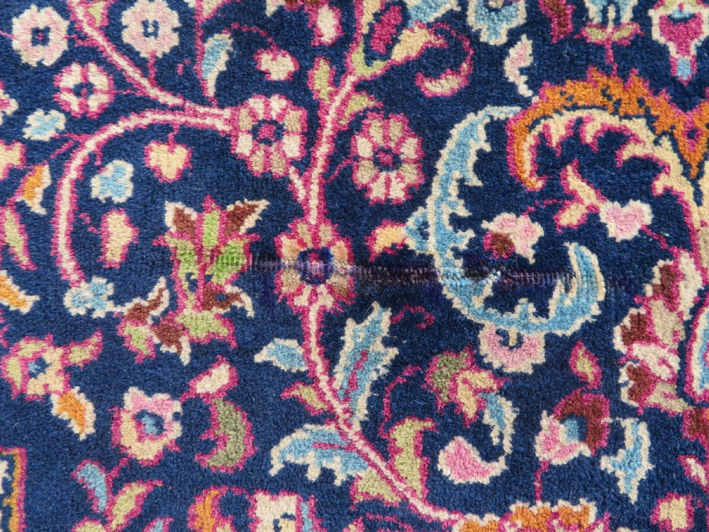 A rectangular hand-knotted wool rug featuring a central indigo floral medallion, cream spandrels, and a magenta border. View VI