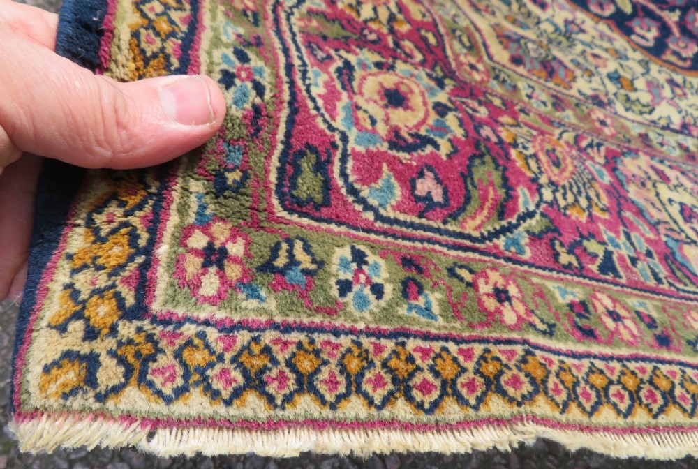 A rectangular hand-knotted wool rug featuring a central indigo floral medallion, cream spandrels, and a magenta border. View VII