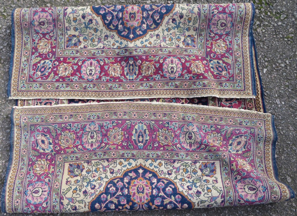 A rectangular hand-knotted wool rug featuring a central indigo floral medallion, cream spandrels, and a magenta border. View X
