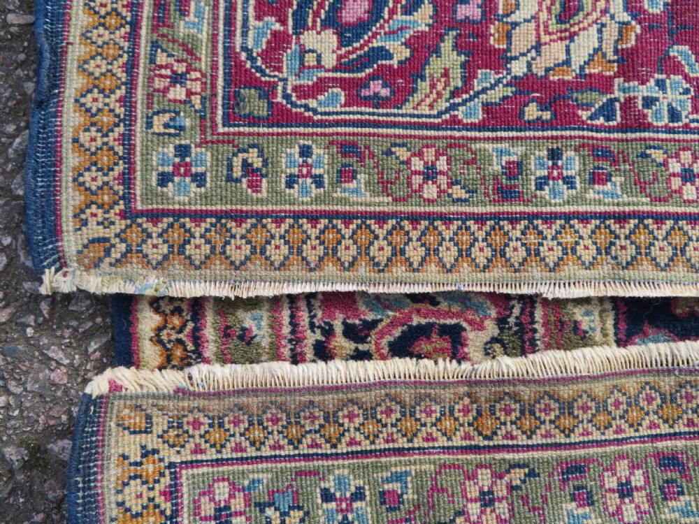 A rectangular hand-knotted wool rug featuring a central indigo floral medallion, cream spandrels, and a magenta border. View XI