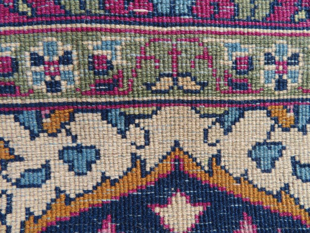 A rectangular hand-knotted wool rug featuring a central indigo floral medallion, cream spandrels, and a magenta border. View XII