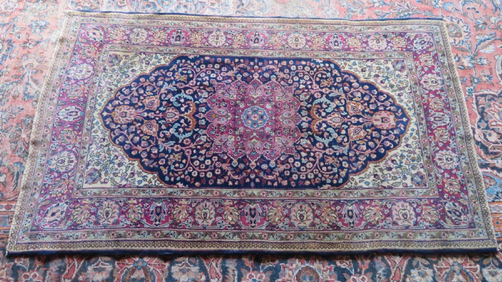 A rectangular hand-knotted wool rug featuring a central indigo floral medallion, cream spandrels, and a magenta border. View XIV