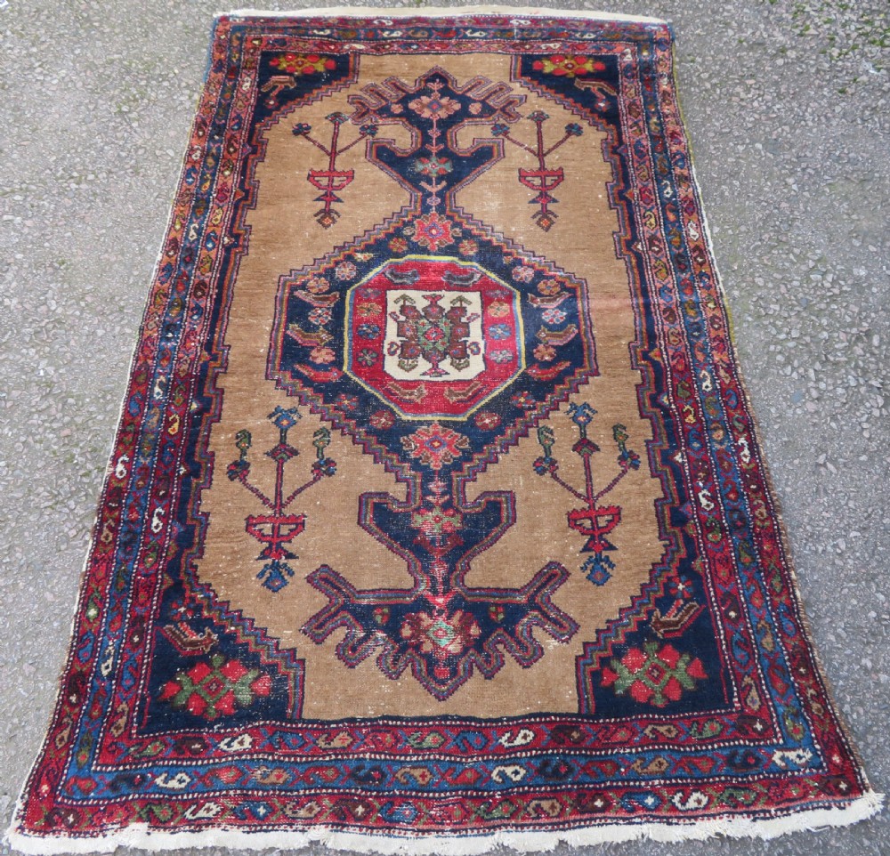 An antique hand-knotted Persian Hamadan wool rug featuring a geometric central medallion on a camel field with navy and red accents.