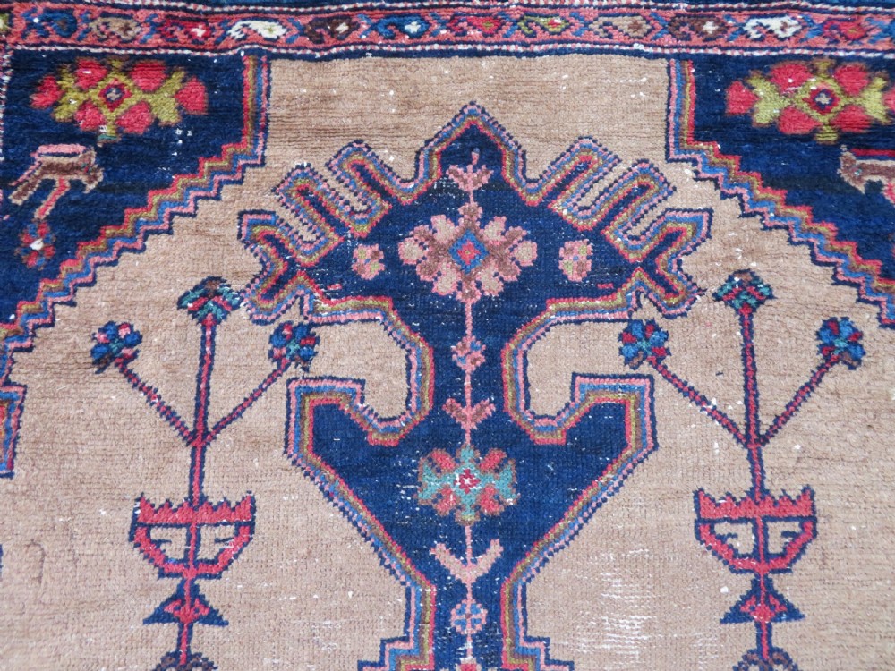 An antique hand-knotted Persian Hamadan wool rug featuring a geometric central medallion on a camel field with navy and red accents. View V