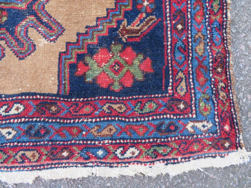 An antique hand-knotted Persian Hamadan wool rug featuring a geometric central medallion on a camel field with navy and red accents. View IX