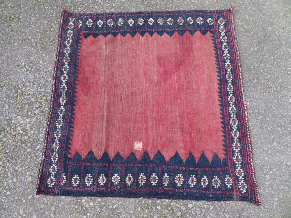 A square antique Afshar flatweave sofreh rug with a faded red central field and serrated indigo blue geometric borders. View II