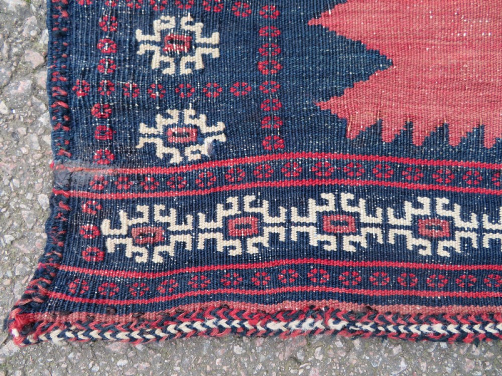 A square antique Afshar flatweave sofreh rug with a faded red central field and serrated indigo blue geometric borders. View III