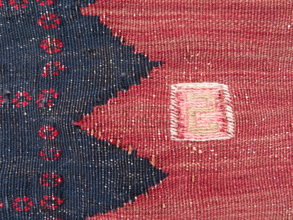 A square antique Afshar flatweave sofreh rug with a faded red central field and serrated indigo blue geometric borders. View IV
