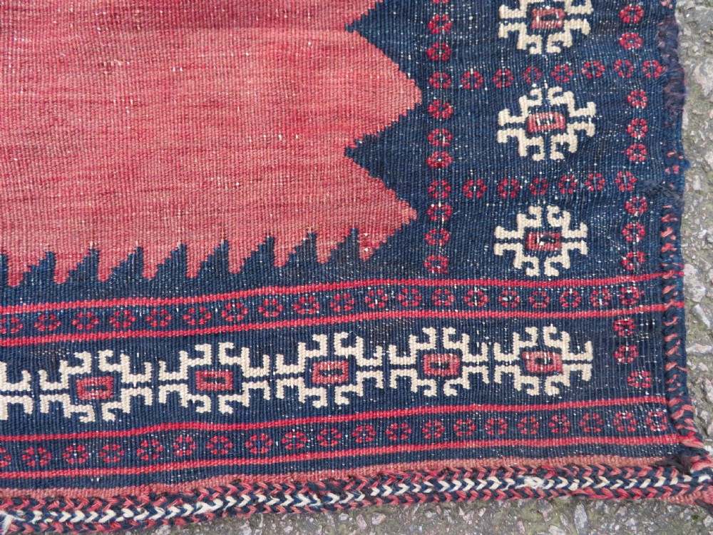 A square antique Afshar flatweave sofreh rug with a faded red central field and serrated indigo blue geometric borders. View V
