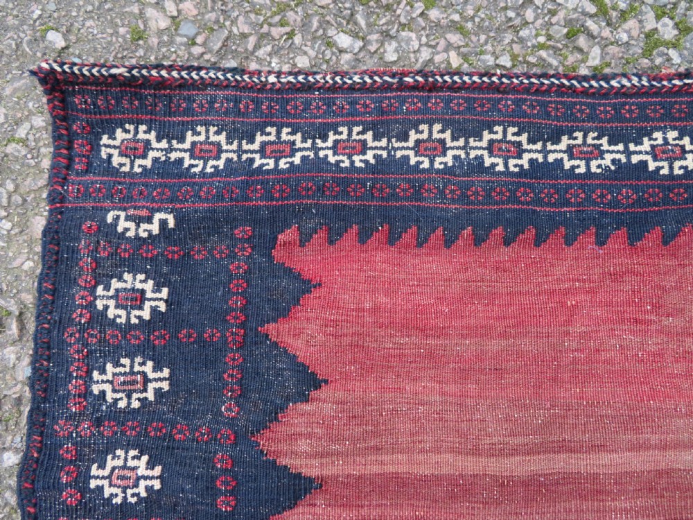 A square antique Afshar flatweave sofreh rug with a faded red central field and serrated indigo blue geometric borders. View VI