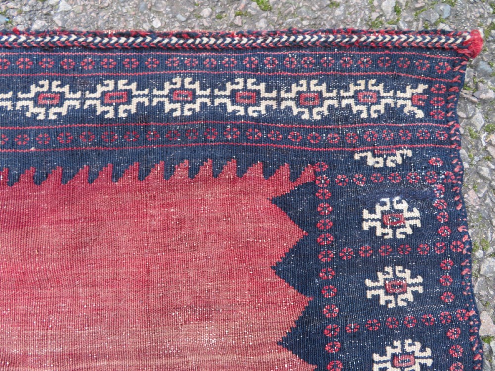 A square antique Afshar flatweave sofreh rug with a faded red central field and serrated indigo blue geometric borders. View VII