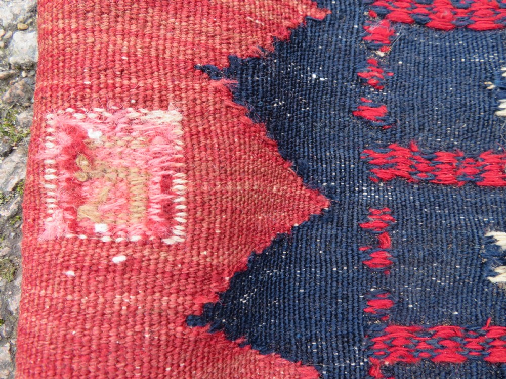 A square antique Afshar flatweave sofreh rug with a faded red central field and serrated indigo blue geometric borders. View X