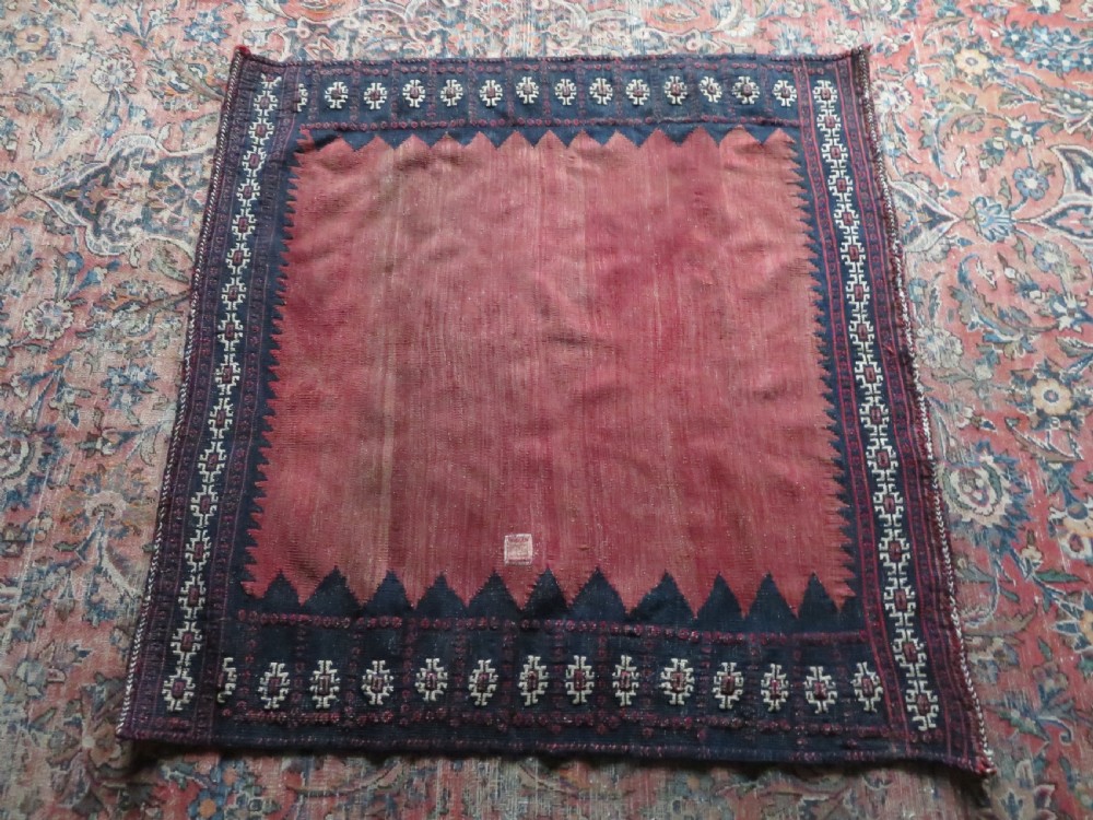 A square antique Afshar flatweave sofreh rug with a faded red central field and serrated indigo blue geometric borders. View XII