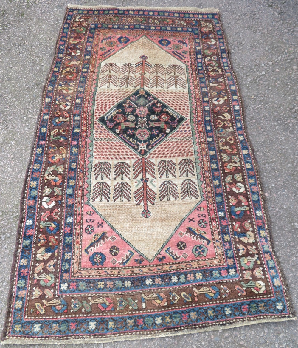 An antique Kurdish tribal rug featuring a cream field with stylized tree motifs, a central navy diamond medallion, and terracotta pink geometric borders.
