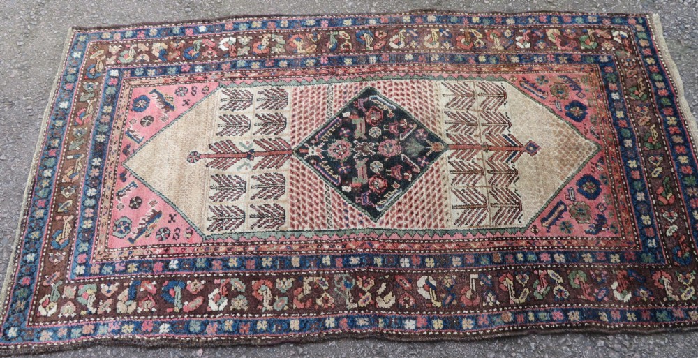 An antique Kurdish tribal rug featuring a cream field with stylized tree motifs, a central navy diamond medallion, and terracotta pink geometric borders. View II
