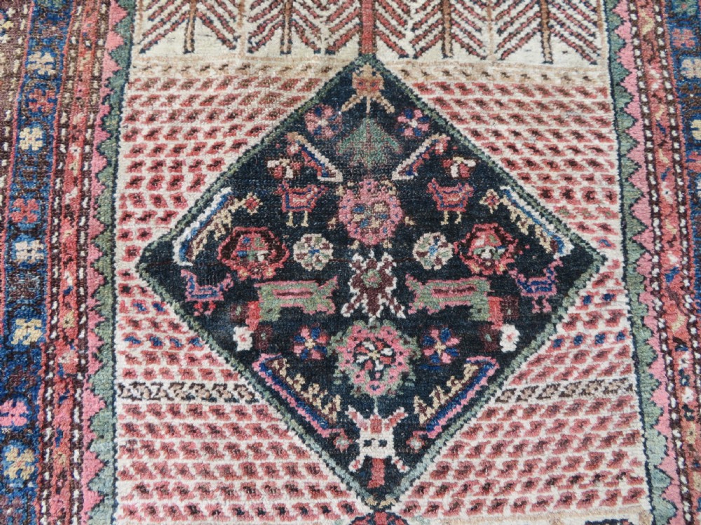 An antique Kurdish tribal rug featuring a cream field with stylized tree motifs, a central navy diamond medallion, and terracotta pink geometric borders. View III
