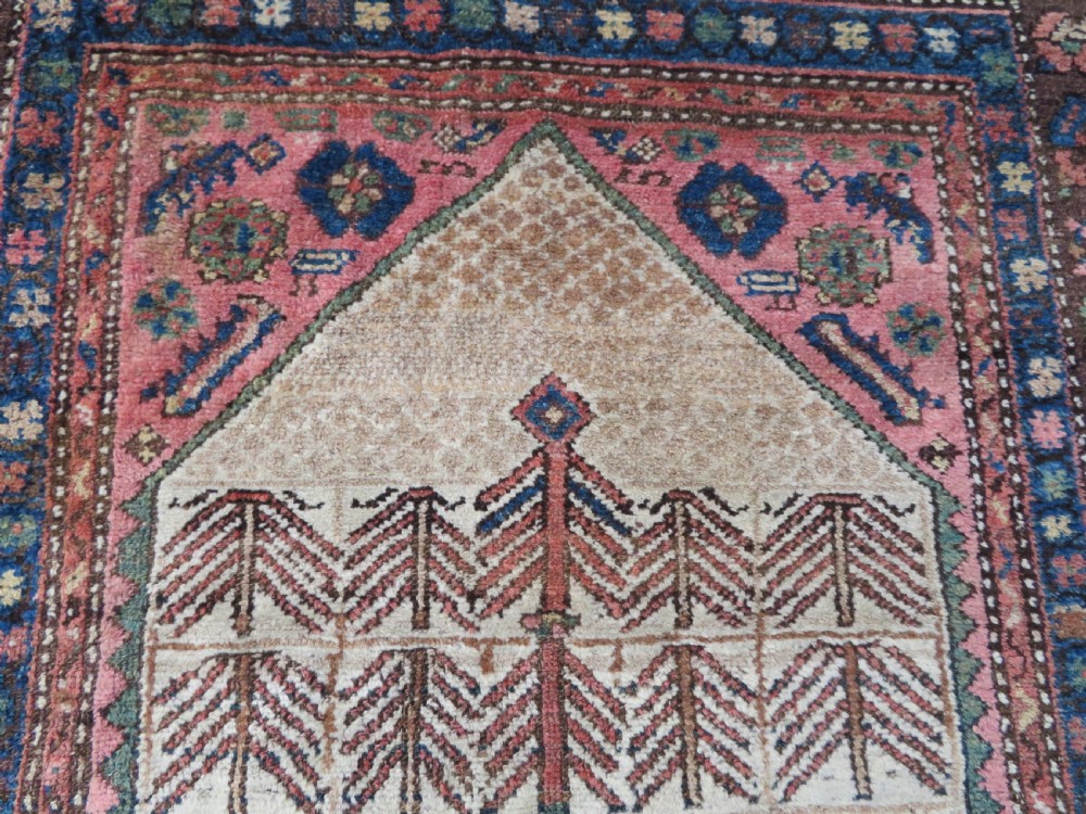 An antique Kurdish tribal rug featuring a cream field with stylized tree motifs, a central navy diamond medallion, and terracotta pink geometric borders. View V