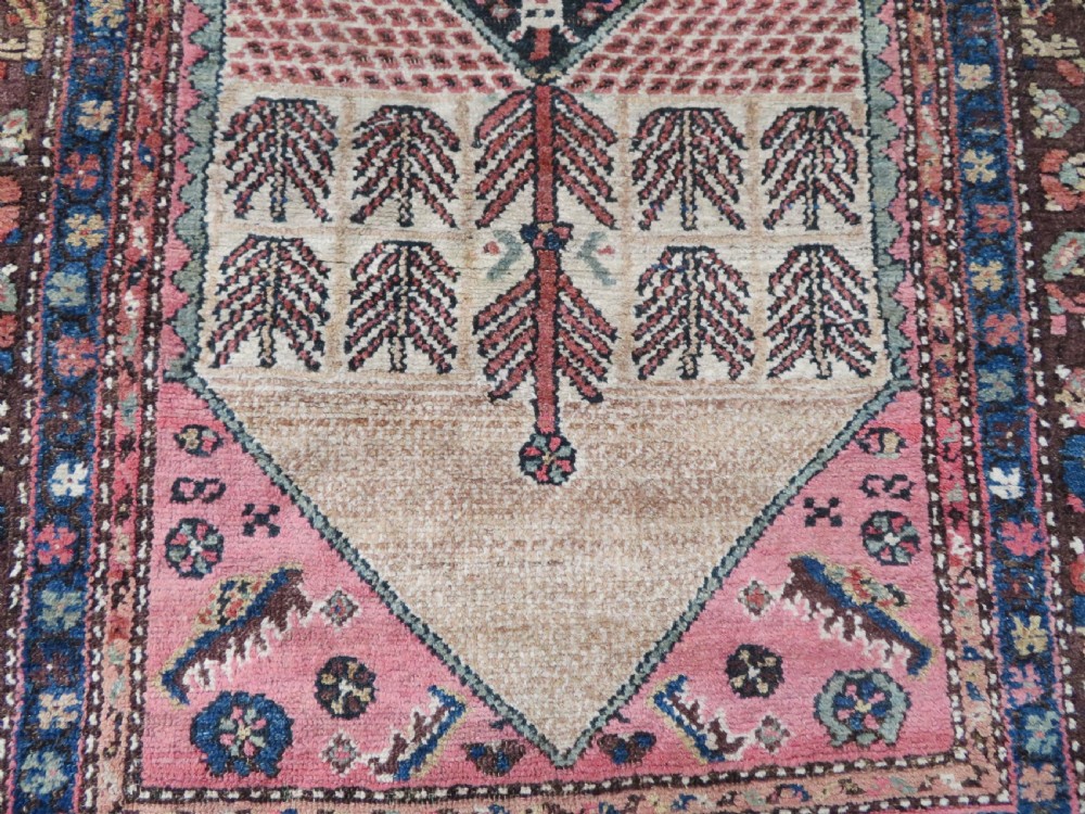 An antique Kurdish tribal rug featuring a cream field with stylized tree motifs, a central navy diamond medallion, and terracotta pink geometric borders. View VI