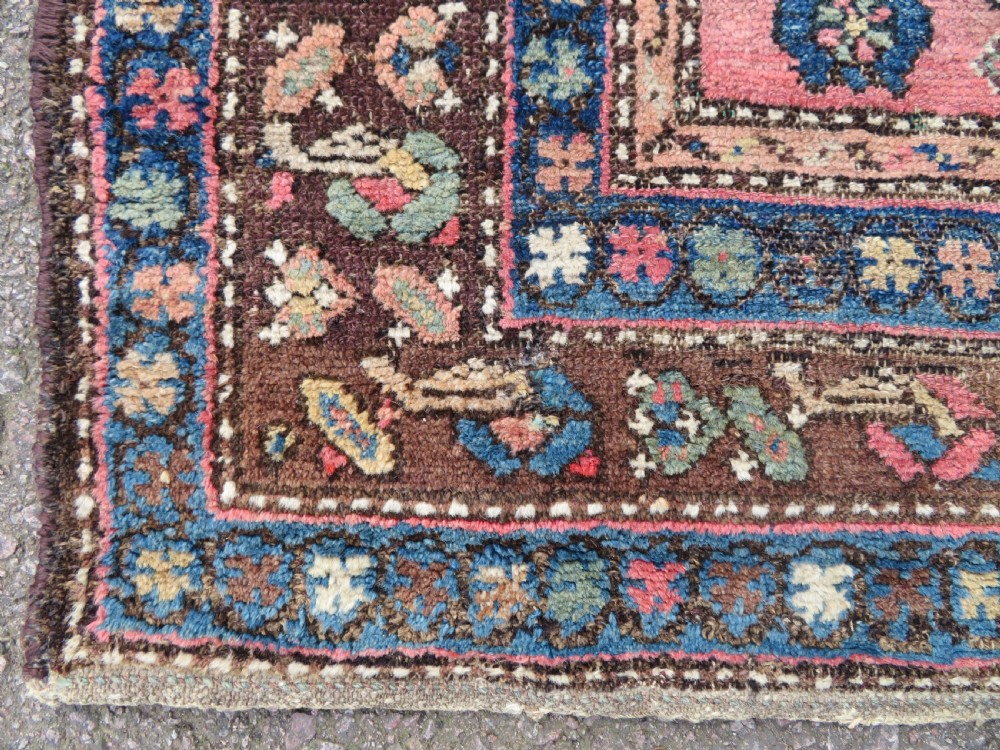 An antique Kurdish tribal rug featuring a cream field with stylized tree motifs, a central navy diamond medallion, and terracotta pink geometric borders. View VII