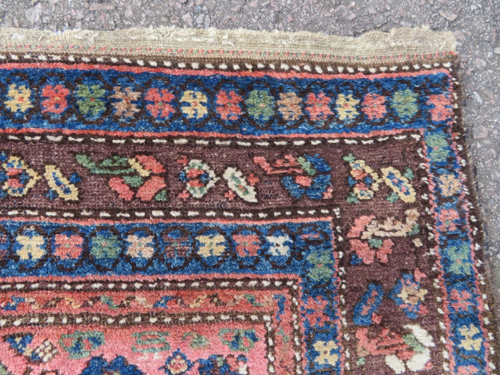 An antique Kurdish tribal rug featuring a cream field with stylized tree motifs, a central navy diamond medallion, and terracotta pink geometric borders. View X