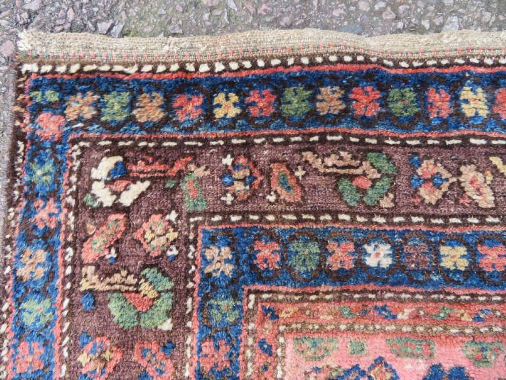 An antique Kurdish tribal rug featuring a cream field with stylized tree motifs, a central navy diamond medallion, and terracotta pink geometric borders. View XI
