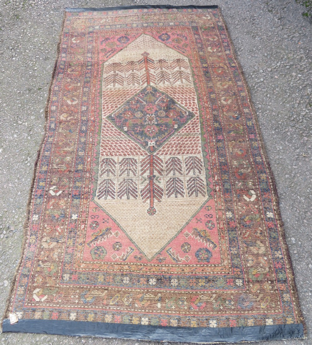 An antique Kurdish tribal rug featuring a cream field with stylized tree motifs, a central navy diamond medallion, and terracotta pink geometric borders. View XIII