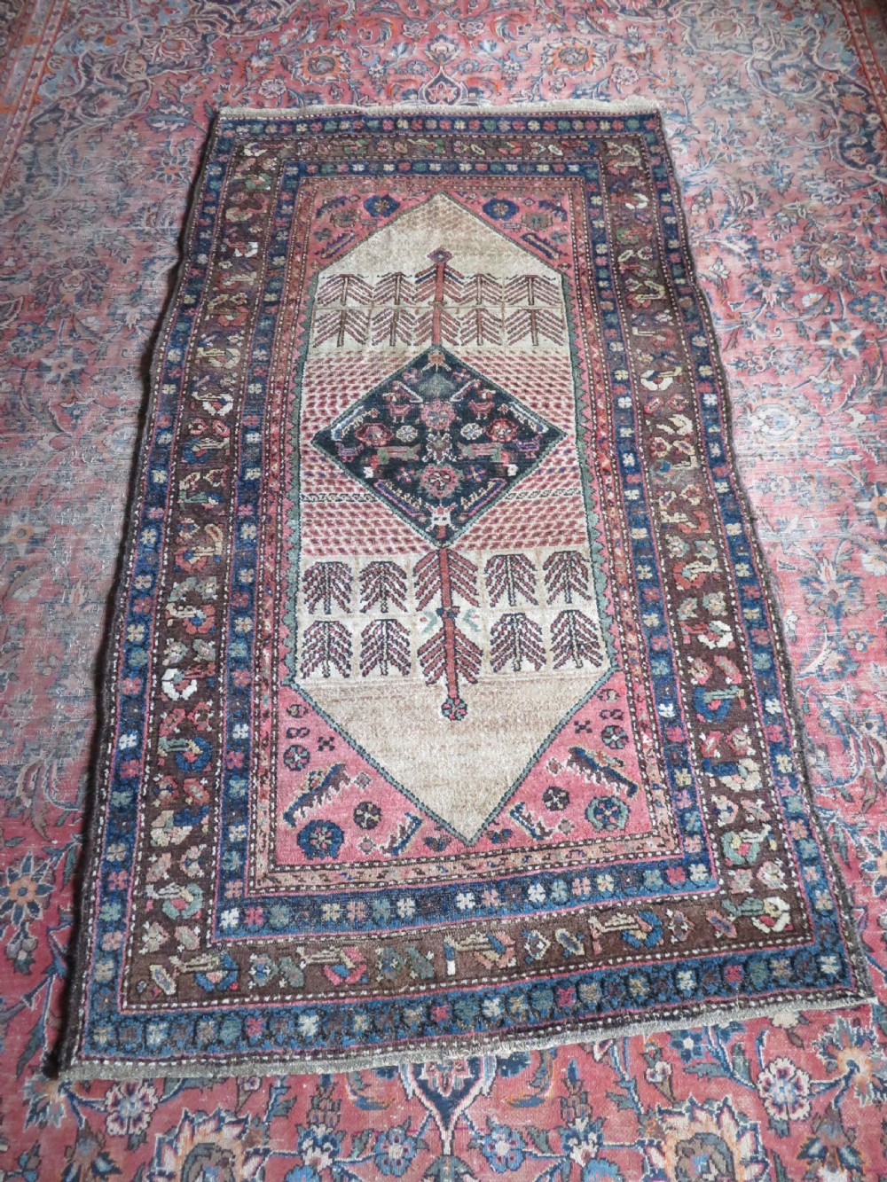 An antique Kurdish tribal rug featuring a cream field with stylized tree motifs, a central navy diamond medallion, and terracotta pink geometric borders. View XVI