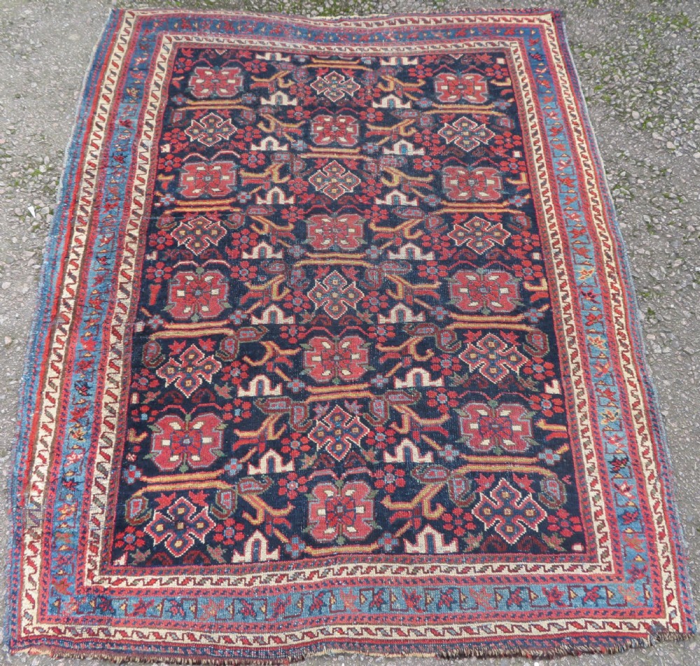 A rectangular hand-knotted antique Afshar rug featuring geometric floral motifs in terracotta red and sky blue on a deep navy blue background.