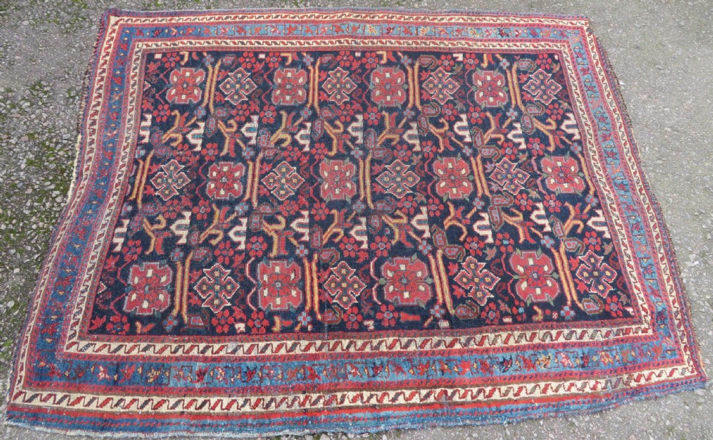 A rectangular hand-knotted antique Afshar rug featuring geometric floral motifs in terracotta red and sky blue on a deep navy blue background. View II